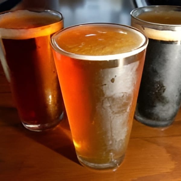 Three glasses of beer, two amber and one dark, with foamy tops on a wooden table.
