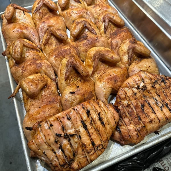 A tray filled with many whole roasted chickens and grilled chicken breasts, seasoned and golden brown.