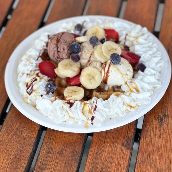 A waffle dessert with chocolate and vanilla ice cream, bananas, strawberries, blueberries, and whipped cream.